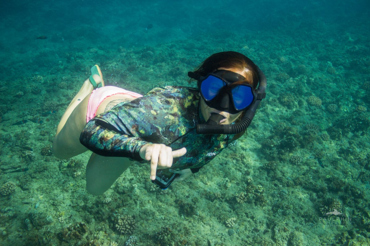 A crew member underwater throwing a shaka